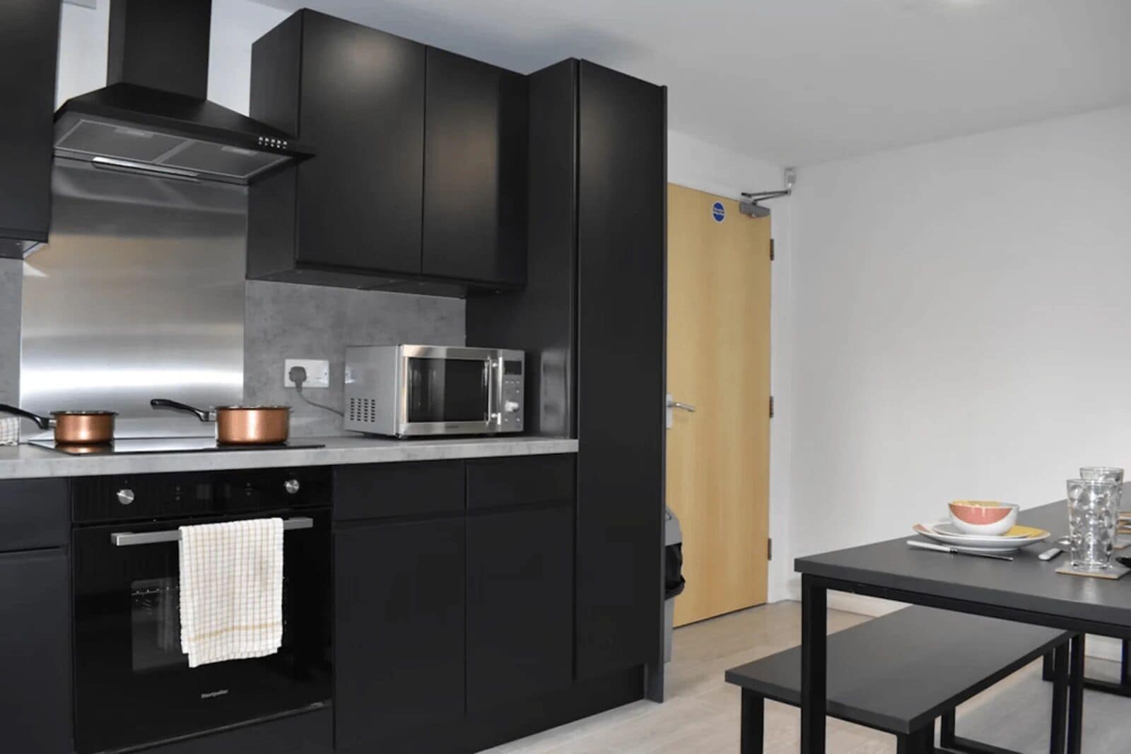 A modern kitchen with black cabinets, stainless steel appliances, and a wooden door.