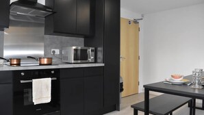 A modern kitchen with black cabinets, stainless steel appliances, and a wooden door. - Student Only Queens Court (Leicester)