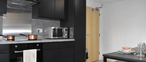 A modern kitchen with black cabinets, stainless steel appliances, and a wooden door.