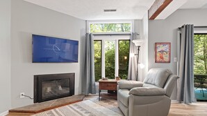 A modern living room with a fireplace, a sofa, a coffee table, and a large window with curtains. - Three Ridges 64 With Wintergreen Advantage (Wintergreen)