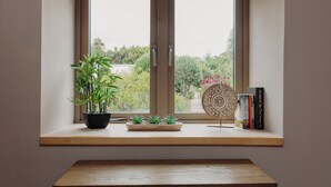 Una ventana con vistas a follaje, una planta en maceta y un objeto decorativo en un repisa.