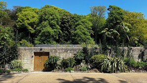 Un edificio de piedra con puerta de madera, rodeado de abundante vegetación y árboles.