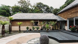Una casa moderna con fachada de madera, un patio empedrado y diversas plantas en macetas.
