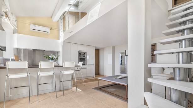 A modern kitchen with white cabinetry, a dining area with a table and chairs, and a mezzanine level with shelves. - Charming 2-Bed Appartment in the heart of Mougins with AC, near Cannes (Mougins)