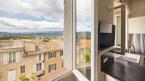 A room with a large window overlooking a cityscape, a flat-screen TV, and a modern kitchen area. - Charming 2-Bed Appartment in the heart of Mougins with AC, near Cannes (Mougins)