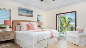 A bedroom with a large bed, a nightstand, a chair, and a view of palm trees through a large window. - Villa La Percha With 4 Bedrooms and 4 5 Bathrooms (Providenciales)
