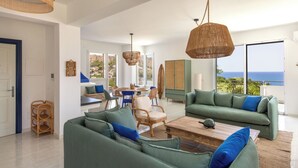 A spacious living area with a green sofa, wicker chairs, a wooden coffee table, and a view of the ocean. - Sea Frame Design Apartments with Pool by Wonderful Italy (Santa Flavia)