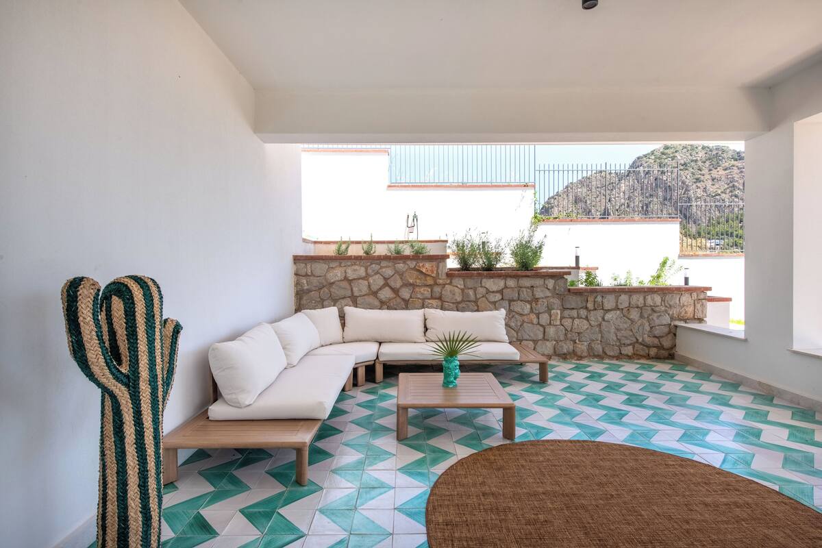 A modern living room with a stone wall, a wooden sofa, a coffee table, and a cactus sculpture.