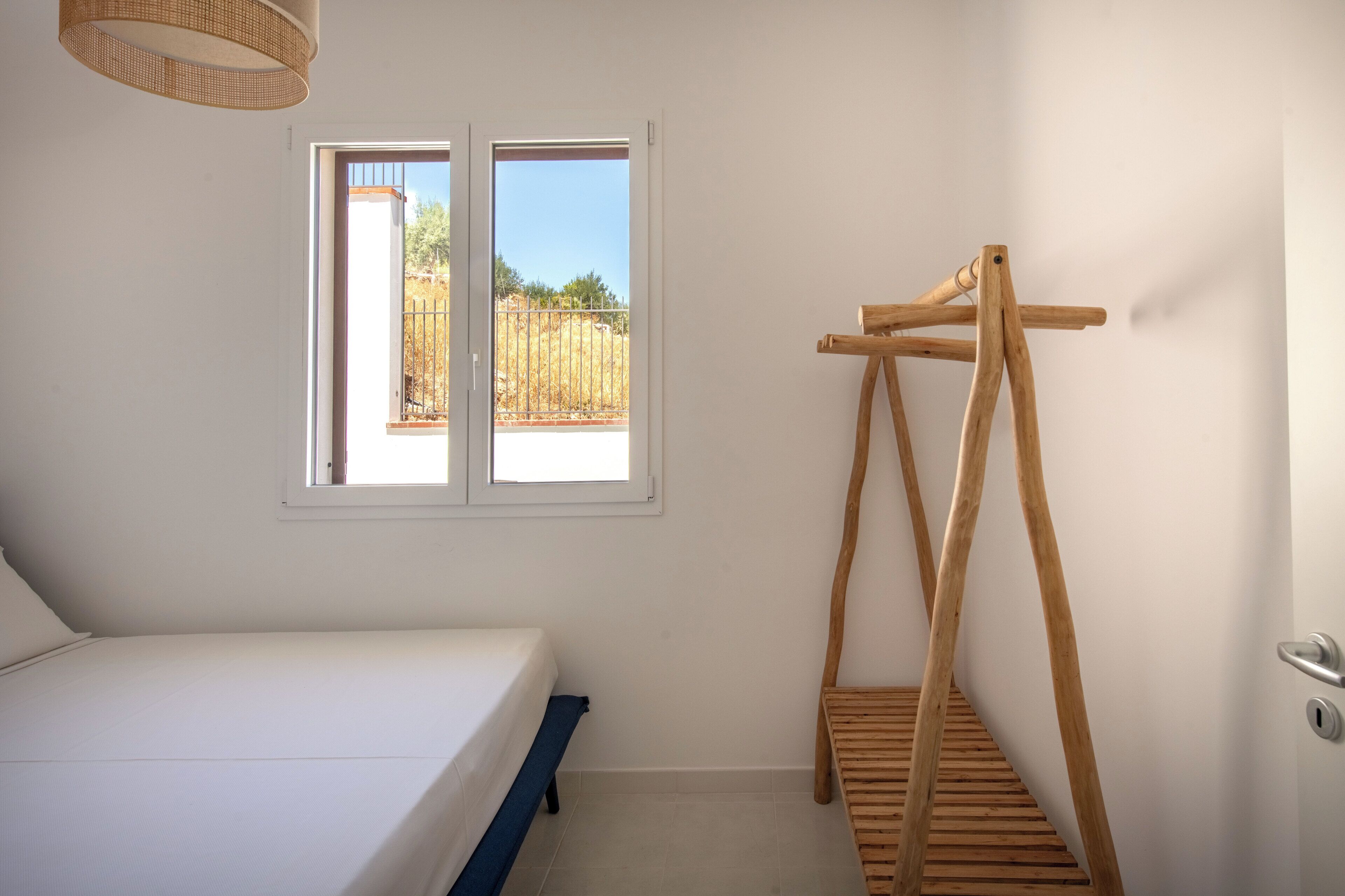 A bedroom with a bed, a window, and a wooden drying rack.