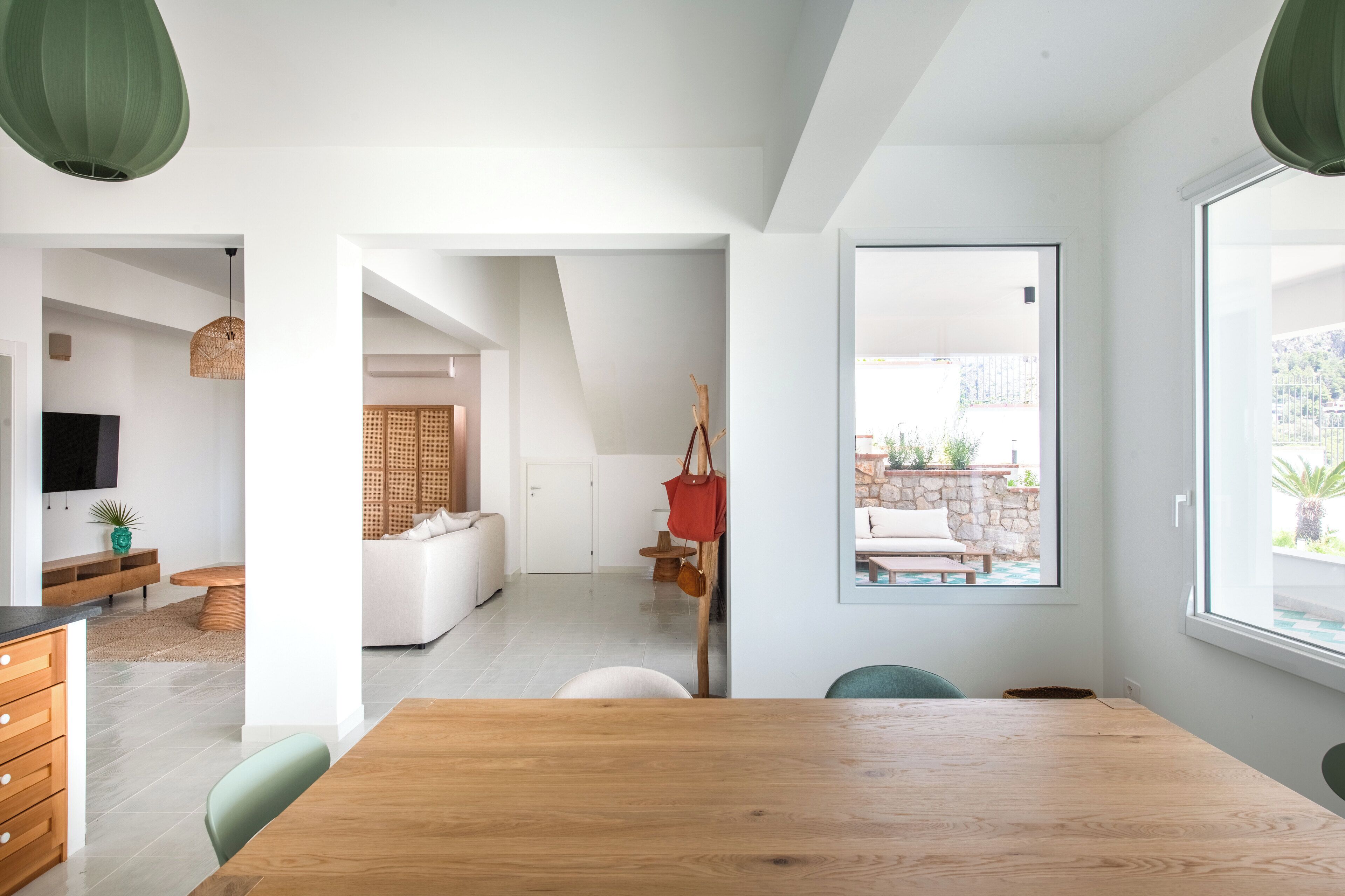 A modern living room with a wooden dining table, a sofa, and a TV. There is a large window with a view of the outdoors.