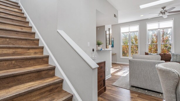 A staircase with wooden steps and white railings, leading to a room with a gray sofa and a large window with autumn foliage view. - Downtown Condo - 2BR, 2BA, Walk to Everything! (Raleigh)
