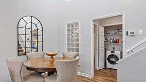 A dining area with a round table and chairs, a large mirror, and a view into a laundry room with a washing machine and shelves. - Downtown Condo - 2BR, 2BA, Walk to Everything! (Raleigh)