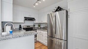 A modern kitchen with white cabinets, stainless steel appliances, a granite countertop, and a built-in oven. - Downtown Condo - 2BR, 2BA, Walk to Everything! (Raleigh)