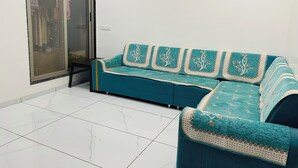 Ein blaugrünes Sofa mit aufwendigen Mustern, eine Schiebetür aus Glas und ein Deckenventilator in einem Raum mit weiß gefliestem Boden.