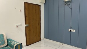 Ein Zimmer mit Holztür, blauer Wand, weiß gefliestem Boden und einem gemusterten Sofa.