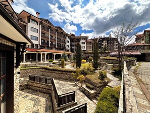Un patio con senderos de piedra, una zona de estar cubierta y edificios de varios pisos con balcones.