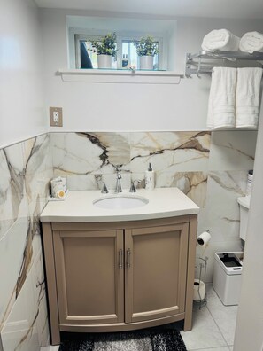 Un baño con salpicadero de mármol, un lavabo y una ventana con plantas.