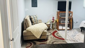 Una sala de estar con sofá, mesa de centro, televisor sobre un mueble, estantería y una puerta.