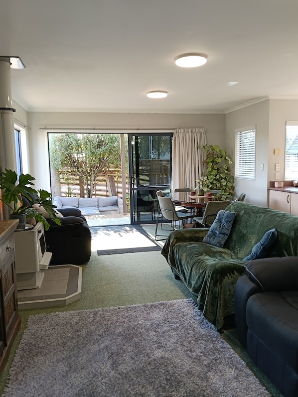Una sala de estar moderna con un sofá, una mesa de comedor y un amplio ventanal corredero que da a un patio.