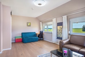 Une pièce avec un plancher en bois, un canapé bleu, un canapé marron, un bureau et une fenêtre donnant sur un paysage verdoyant.