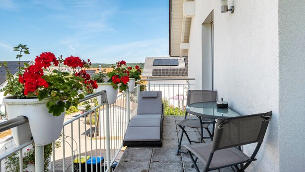 A balcony with potted red flowers, a glass table, and two chairs. - Apartment "Haus Rosengarten" with Balcony and Wi-Fi (Friedenweiler)
