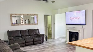 A modern living room with a sectional sofa, a flat-screen TV, a fireplace, and a ceiling fan. - Charming 3-bedroom minutes from OWA (Foley)