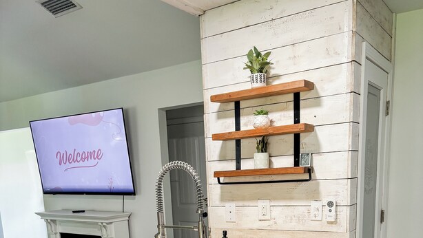 A modern kitchen with a wooden countertop, white cabinetry, a built-in dishwasher, and a wall-mounted TV displaying "Welcome". - Charming 3-bedroom minutes from OWA (Foley)