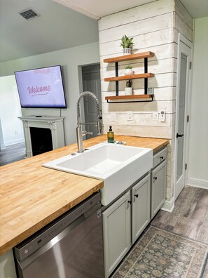 A kitchen with a wooden countertop, a built-in dishwasher, a sink, and a television displaying 'Welcome'. - Charming 3-bedroom minutes from OWA (Foley)