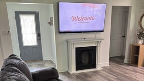 A living room with a dark brown sofa, a fireplace, and a TV displaying "Welcome". - Charming 3-bedroom minutes from OWA (Foley)