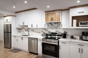 A modern kitchen with white cabinets, a stainless steel refrigerator, a dishwasher, a stove, and a microwave. - 20 Min Airport|Spacious 2BR Suite| Modern| Bright (Beaumont)