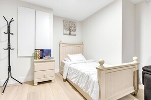 Een slaapkamer met een bed, een nachtkastje, een kapstok en een aan de muur hangend schilderij.