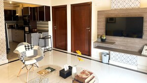 Una sala de estar moderna con televisor, comedor con barra y cocina con gabinetes oscuros.