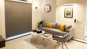 Una sala de estar moderna con sofá, mesa de centro, alfombra estampada y un reloj en la pared.