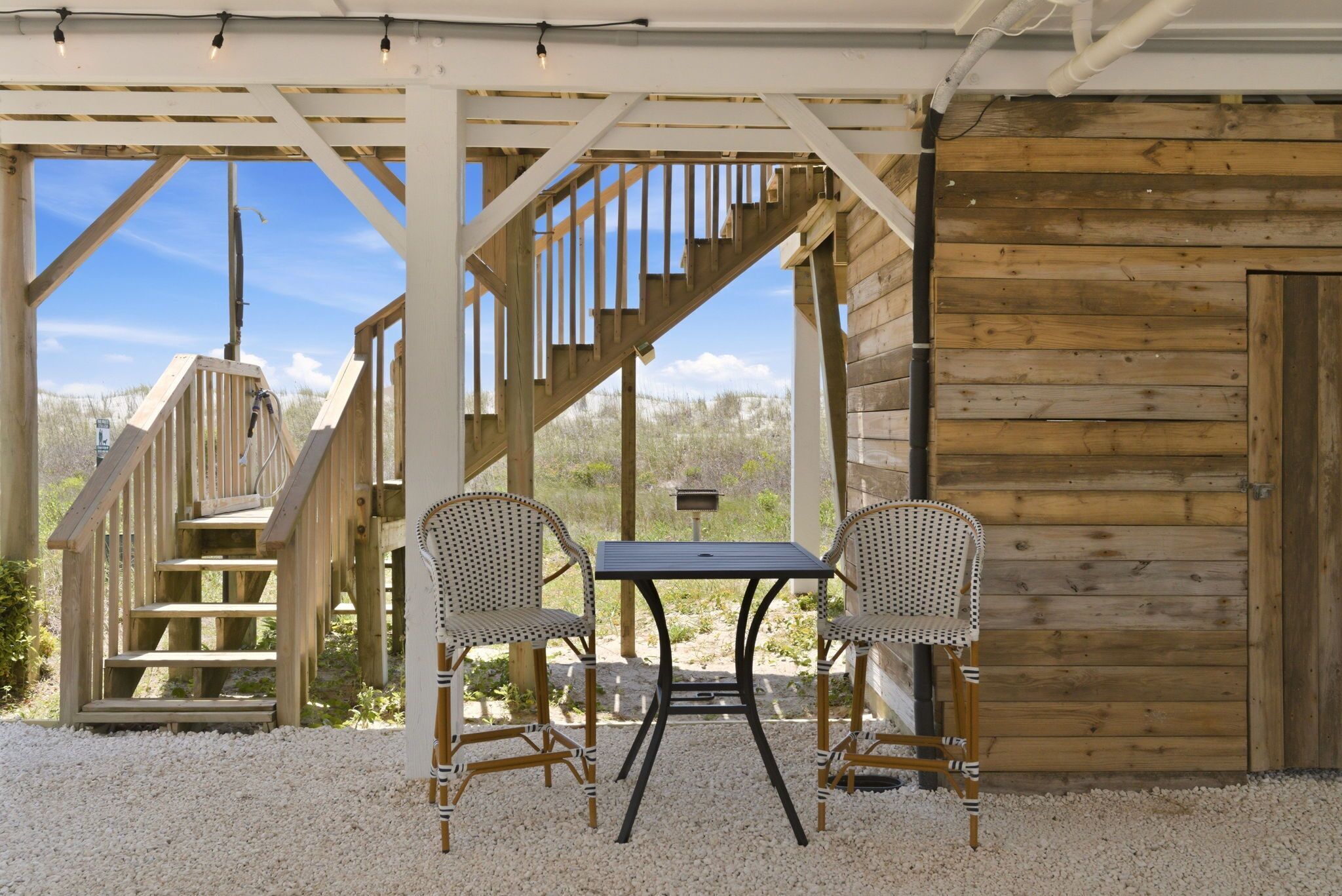 Un espace extérieur abrité, aménagé avec une table et deux chaises en osier, un escalier en bois et un mur en bois.