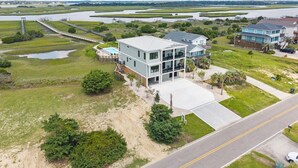 A modern two-story house with a large balcony, a swimming pool, and a view of a river and marshland.