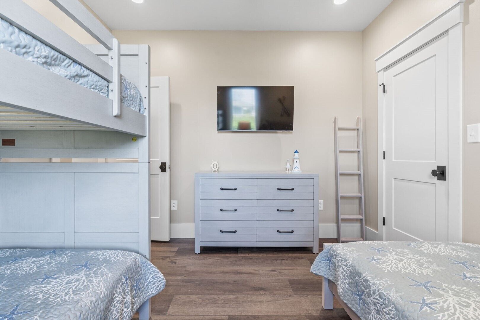 Une chambre avec des lits superposés, une commode, un téléviseur et une porte.