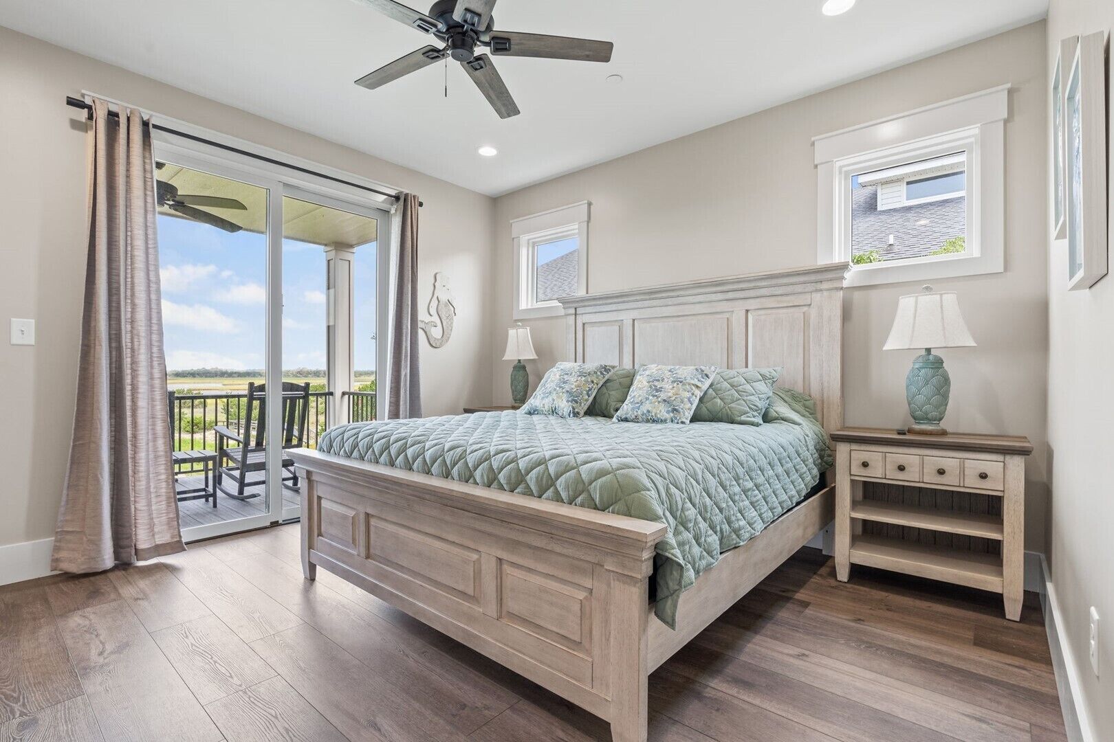 A bedroom with a bed, a nightstand, a ceiling fan, and a view of the outdoors.