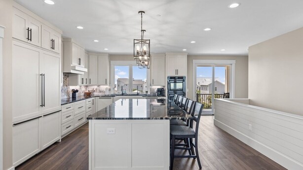 A spacious kitchen with a large island, white cabinetry, and a chandelier.