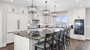 A modern kitchen with white cabinetry, a large island with bar stools, and built-in appliances.