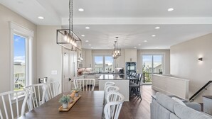 A spacious kitchen with white cabinetry, a central island, and a dining area with white chairs.