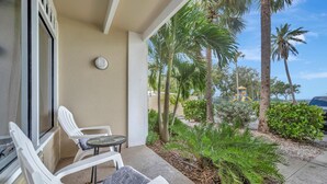 A balcony with white plastic chairs and a small table, overlooking a garden with palm trees and a yellow structure. - The Beach! | Pool, Hot Tub, Gym, Game Room, Tennis (Ruskin)