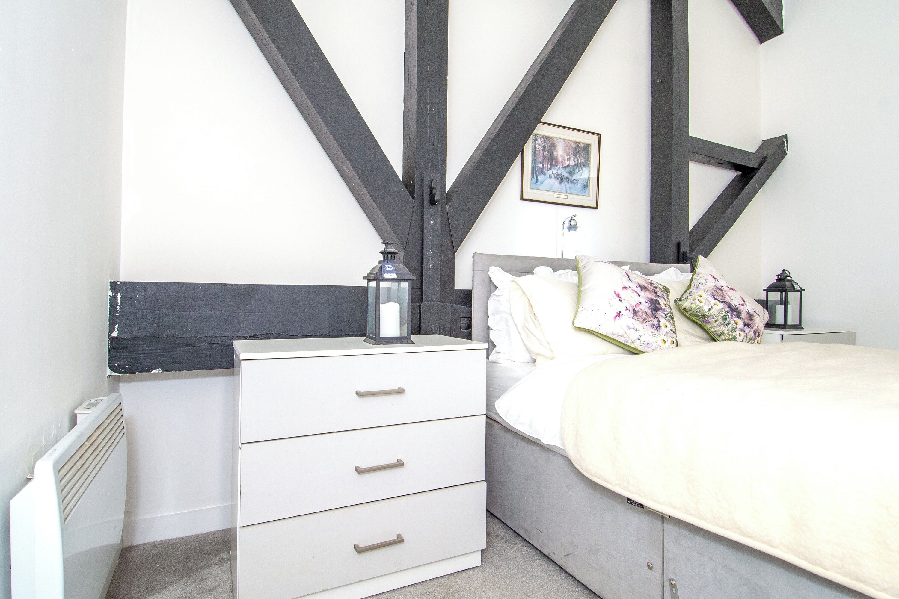 A bedroom with a bed, a nightstand, a dresser, and a radiator.