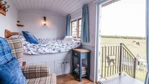 Een knus vertrek met een bed, een bank, een klein tafeltje en uitzicht op een paard in een veld door een glazen deur.