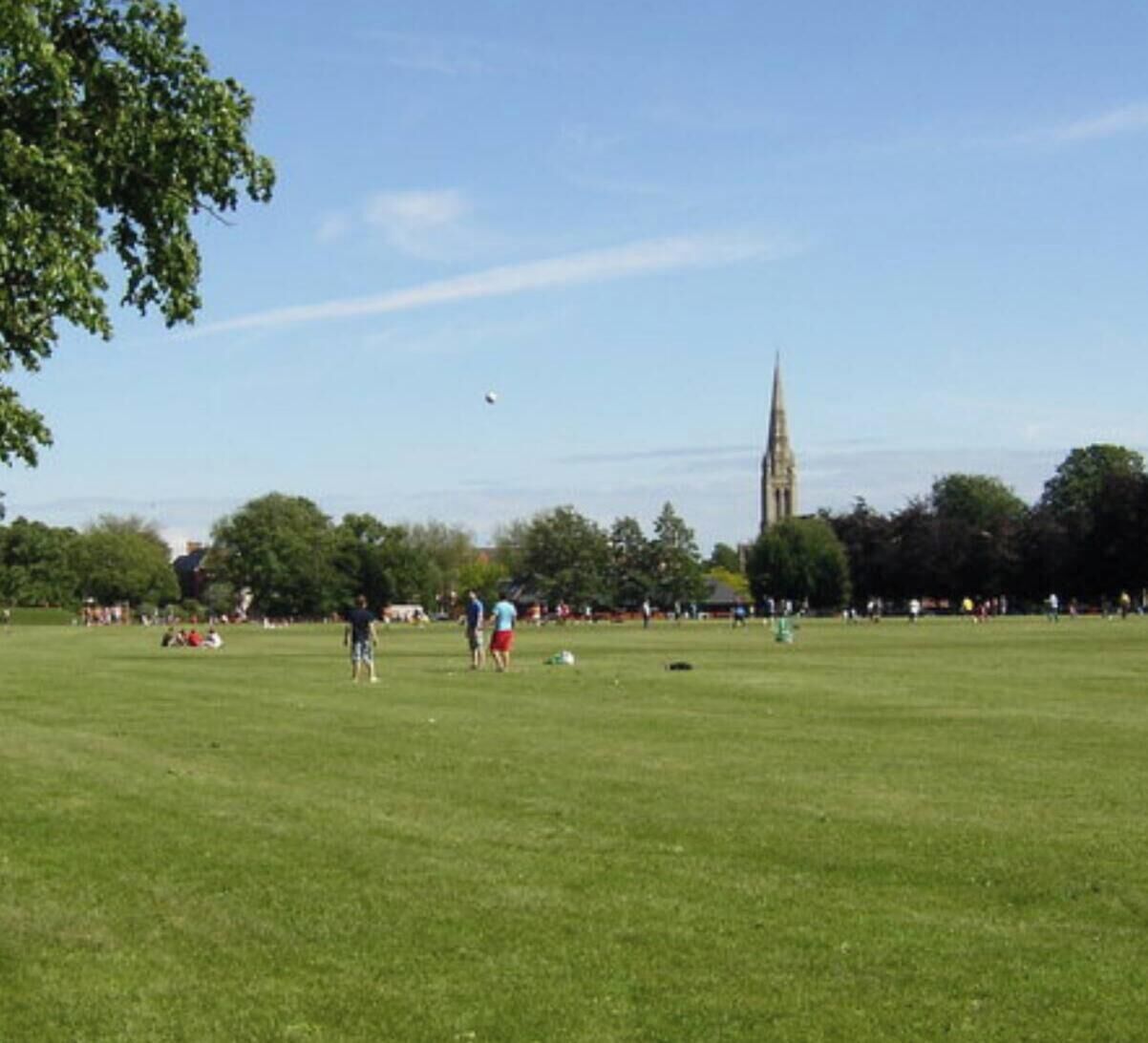 A large open grassy field with a tall church spire in the background.