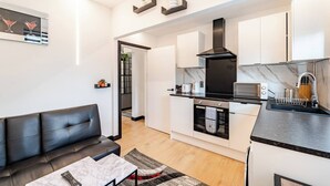 A modern kitchen with white cabinets, a black range hood, and a microwave. There's a black leather sofa and a small table with a remote control. - Modern 1 Bedroom Flat in Aberdeen City Center, With Parking. (Aberdeen)