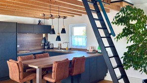 A modern kitchen with a wooden ceiling, a central island with seating, and a black ladder.