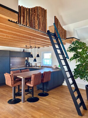 A modern kitchen with a wooden ceiling, a central island with seating, and a black ladder. - Beautiful large vacation apartment with private terrace in the Hunsrück. 70 sqm (Norath)