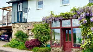 A two-story building with a stone facade, a red door, and purple wisteria vines.