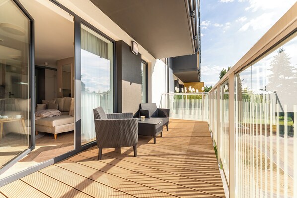 A balcony with a sofa and chairs, a glass door leading to a room, and a view of the outdoors. - BeachTime Apartments & SPA Grzybowo by POSESJA APARTAMENTY (Grzybowo)