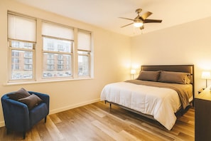 A bedroom with a bed, a chair, a ceiling fan, and windows with blinds. - Pet-Friendly CWE 2BR · King Bed · Pool · Walk to Forest Park & Barnes-Jewish (St. Louis)